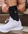 Person wearing white sneakers adjusting 849 Ultra Gel Lace Up Ankle Support With Internal Gel Cushions For All Day Comfort Large Black