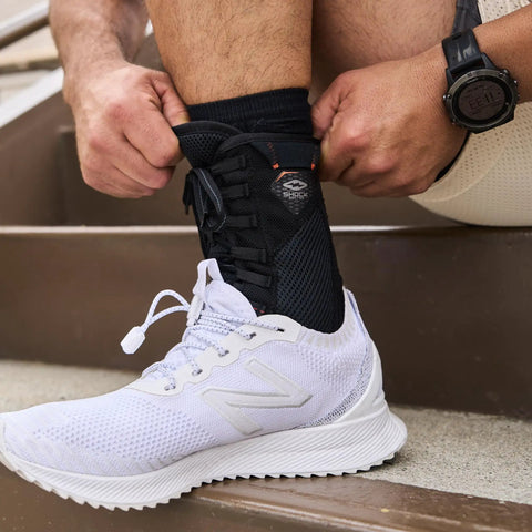 Person wearing white sneakers adjusting 849 Ultra Gel Lace Up Ankle Support With Internal Gel Cushions For All Day Comfort Large Black