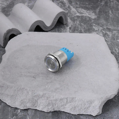 Close-up of Twin Pack 12V IP65 Waterproof LED Flash Buzzer Indicator Light 19mm for electrical panels, blue and silver on stone surface.