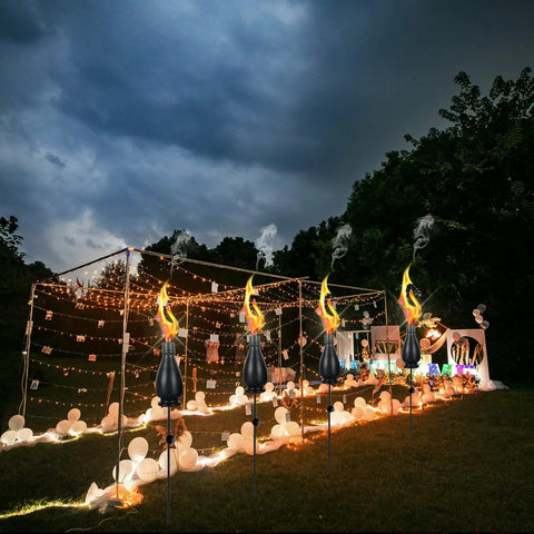 Citronella Torches 6 Pack for Outdoor Lighting, 60 Inch Jet Black Metal Pathway Torches at night, illuminating a garden event.