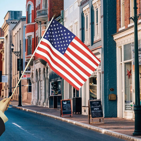 Person holding All American Flags On Sticks 12 By 18 Inch 12 Pack With 6 World Cup Themed Flags, preassembled outdoor flag on street.