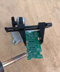 Pro Grade Junior Miniature Vise With One Knob Head Control holding a PCB for precise soldering on wooden tabletop.