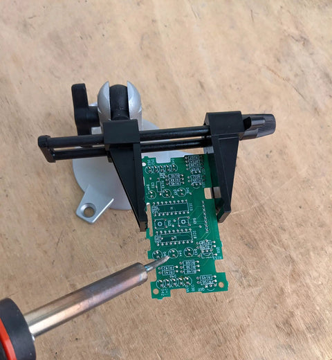Pro Grade Junior Miniature Vise With One Knob Head Control holding a PCB for precise soldering on wooden tabletop.