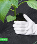 Gloved hand installing Heavy Duty Weed Barrier Fabric 3ft By 300ft 3.2oz Tear-Resistant Ground Cover around plant stem.