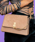 Close-up of a stylish suede purse held by a model, showcasing the chain strap and clasp detail.