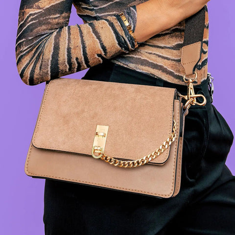 Close-up of a stylish suede purse held by a model, showcasing the chain strap and clasp detail.