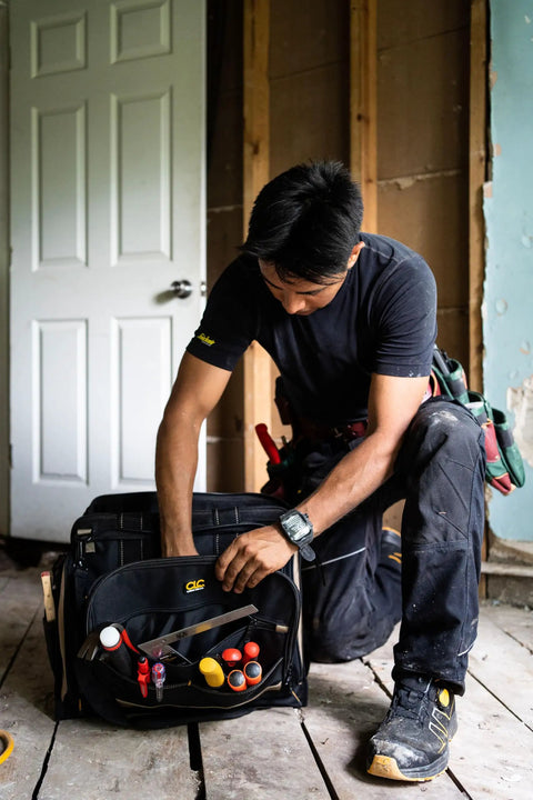 Man reaching into Heavy Duty Tool Bag With 50 Pockets And Large Center Compartment, Multi-Compartment Tool Organizer For Power Tools.