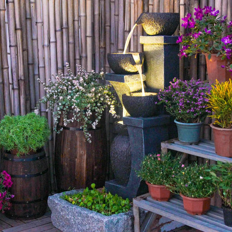 Four Bowl Outdoor Water Fountain With LED Lights Modern Polyresin Floor Fountain for Garden and Patio surrounded by plants