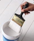 Person holding 4 Inch Soft Tip Paint Brush For Walls And Trim With Pro Grade Synthetic Bristles That Hold More Paint For Fewer Strokes over paint bucket