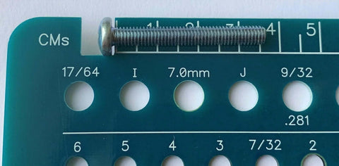 Close-up of blue-green Holistic drill bit gauge with three sizes: 17/64 in, 7.0 mm, 9/32 in; metal screw resting on top.