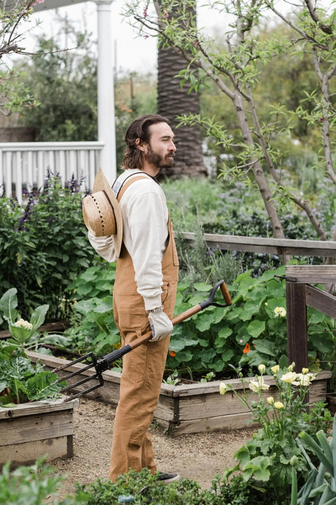 Gardener holding a Foldable Spading Fork For Digging And Aerating Durable Steel Garden Tool in a lush home garden setting