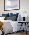 D'Alessio Table Lamp In Matte Black With Modern Cutout Body And White Linen Shade, 20 Inch Tall on a bedside table next to bed.