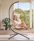 Woman relaxing in a hanging egg chair with stand and footrest for indoor outdoor use, foldable wicker rattan swing chair on patio.
