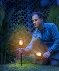 Man installing P2 Solar Flickering Flame Torch Light With Realistic Fire, IP65 Waterproof Outdoor Tiki Lamp in garden at night