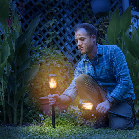 Man installing P2 Solar Flickering Flame Torch Light With Realistic Fire, IP65 Waterproof Outdoor Tiki Lamp in garden at night