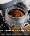Close-up of Luxe Café Premier 3 In 1 Espresso Machine With Built In Grinder Drip Coffee And Rapid Cold Brew Hands Free Milk Frother Assisted Tamper For Cappuccinos And Lattes Stainless Steel showing coffee grounds in grinder.