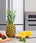 Whole pineapple and diced pieces with V Shape Pineapple Eye Remover Tool With Multipurpose Clip Stainless Steel Peeler on counter.
