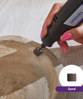 Close-up of Dremel rotary tool sanding wood with a small sanding bit; black handheld tool with blue Dremel label