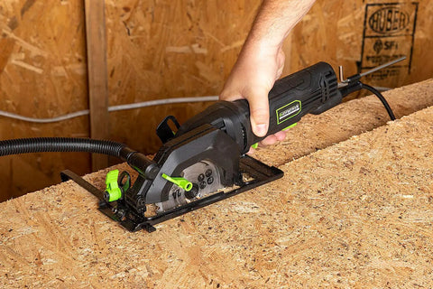 Genesis Mini Circular Saw 4.0 Amp 4-1/2 Inch with 24-Tooth Carbide Blade cutting wood surface with vacuum adapter attached