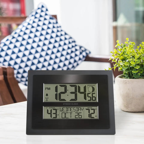 Digital Atomic Clock With Outdoor Temperature And Moon Phase Auto Time Sync Large Two Inch Digits Twelve Or Twenty Four Hour Display DST Auto Seven Time Zones No Fuss Setup Black Wall Or Desk Clock For Home And Office on white table with plant