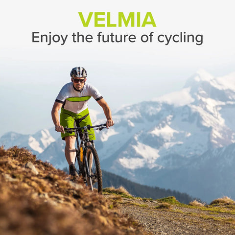 Cyclist on mountain trail wearing helmet and biking gear with mountains in the background.