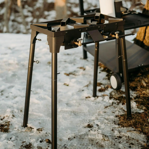 Black Double Propane Camp Burner With Adjustable Height And Removable Legs Four Tier For Outdoor Cooking on snowy ground.