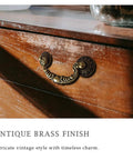 Vintage drop bail cabinet handle in antique brass finish on wooden dresser, showcasing intricate design and timeless style.