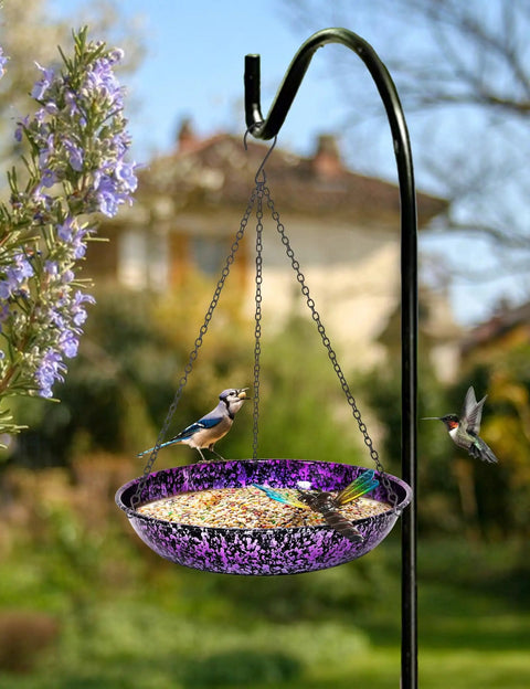 Outdoor 11 Inch Metal Hanging Bird Bath And Feeder With Colorful Purple And Blue Bowl displayed on a black chain in a garden.