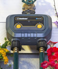 Smart Bluetooth Hose Timer 2 Zone Programmable Watering System with Quick Connect, mounted on wall with garden hoses and flowers