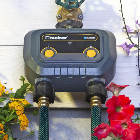 Smart Bluetooth Hose Timer 2 Zone Programmable Watering System with Quick Connect, mounted on wall with garden hoses and flowers