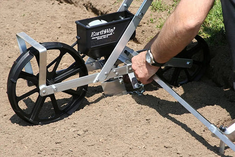 Person using Pro Grade Precision Garden Seeder With 7 Seed Plates For Home Gardeners on prepared soil