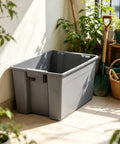 Medium Open Top Stackable Plastic Storage Bin With Reinforced Carry Handles Heavy Duty Gray Utility Tote placed in a garden.