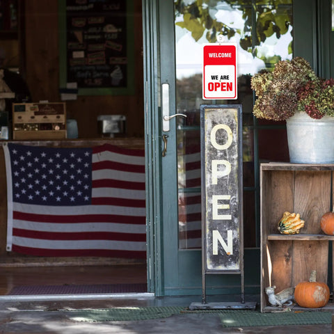 Storefront with 'We Are Open' sign, large 'OPEN' stand, American flag and fall decor near door