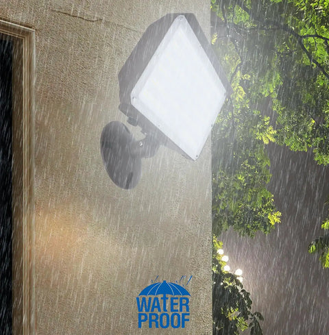 Dusk To Dawn Outdoor 100W LED Flood Light with Knuckle Mount and Wall Plate in rain highlighting waterproof feature.