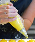 Top Shelf Clear Vinyl Disposable Gloves Straight Up Reliable 3 Mil Thickness used while piping yellow filling in a bakery.