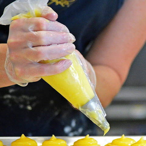 Top Shelf Clear Vinyl Disposable Gloves Straight Up Reliable 3 Mil Thickness used while piping yellow filling in a bakery.