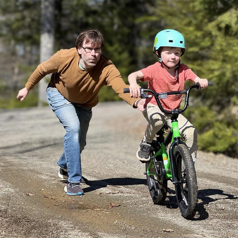 Child on a green 16 Inch Kids Bike For Ages 4 And Up, BMX Style Youth Bicycle With Training Wheels, assisted by an adult.