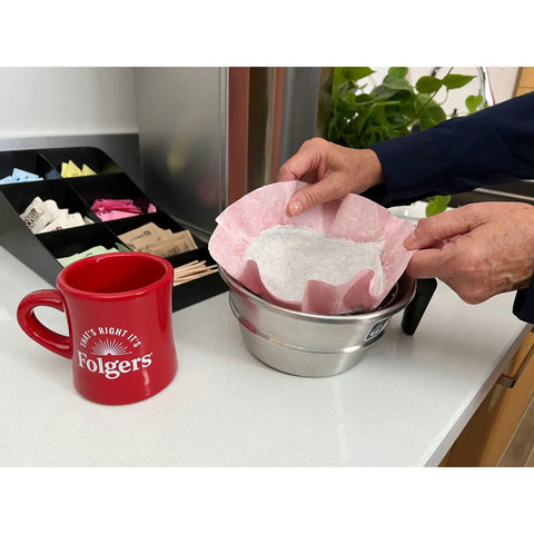 Person placing 0.9 Ounce Caffeine Regular Filter Pack For Easy Premeasured Brews into coffee machine next to red mug on counter
