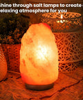 Illuminated Himalayan salt lamp on table with decorative candle holders and plants creating a relaxing atmosphere.