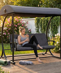 Woman relaxing on All Weather Porch Swing With Canopy And Stand For Outdoor Relaxing 3 Person Patio Swing Bed With Cushions For Yard And Deck Go To Backyard Swing For Adults Grey on a wooden deck