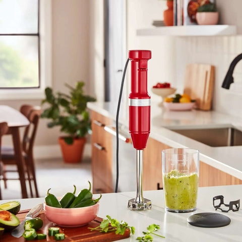Premium Corded Hand Blender Engineered To Easily Whip Up Creamy Smoothies And Silky Soups Fast With Variable Speed Trigger And Removable Stainless Steel Blades In Deep Empire Red Finish on kitchen countertop with avocados and jalapeños.