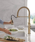Woman using Pro Level Commercial Spring Neck Kitchen Faucet With Magnetic Docking Pull Down Sprayer Diamond Seal Tech in champagne bronze.
