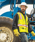 Rock Solid Heavy Duty Reflective Safety Vest Designed For Road Crews And Night Shift Workers Featuring Kickass Ansi Class Two Visibility Cool Airflow Mesh Fabric Six Utility Storage Pockets And Bold Orange Contrast Edging In Extra Large worn by a worker near machinery.