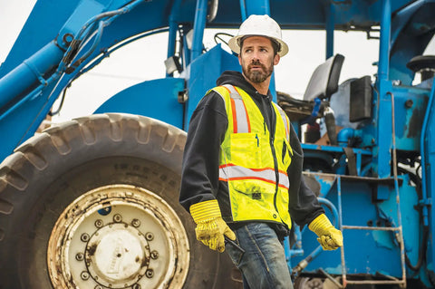 Rock Solid Heavy Duty Reflective Safety Vest Designed For Road Crews And Night Shift Workers Featuring Kickass Ansi Class Two Visibility Cool Airflow Mesh Fabric Six Utility Storage Pockets And Bold Orange Contrast Edging In Extra Large worn by a worker near machinery.