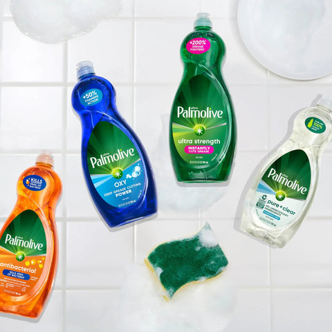 Four Palmolive dish soap bottles, including Oxy Power Degreaser, on a tiled surface with a sponge and white soap bubbles.