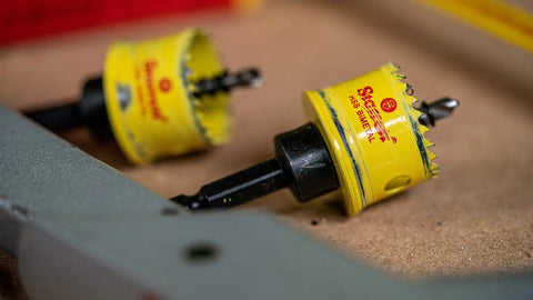 Close-up of Cordless HSS Bi Metal Hole Saw 27mm CSC27 on a workshop table, showing the teeth and alloy body in yellow.
