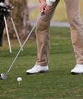 Person standing on golf course preparing to swing, close-up of shoes and golf club near tee.