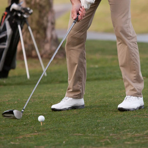 Person standing on golf course preparing to swing, close-up of shoes and golf club near tee.