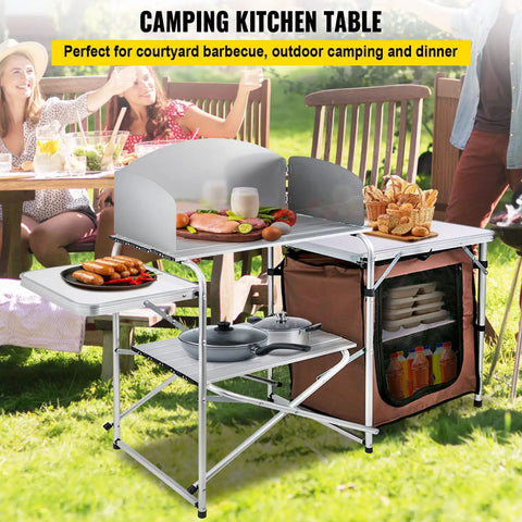 Aluminum Portable Folding Camp Kitchen Table With Windscreen Cupboard And Storage Organizer Carrying Bag For Outdoor Picnics Beach BBQ RV Travel Quick Setup Brown Finish in a picnic setting.