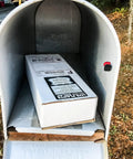 Box package inside an open white metal mailbox on a wooden stand outdoors